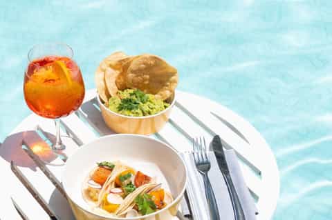 Poolside dining with fish tacos, guacamole, and tropical cocktail on white table
