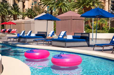 Pool area with blue lounge chairs, pink floats, and palm trees in sunny courtyard setting