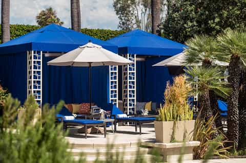 Luxury outdoor lounge area with blue umbrellas, seating, and palm trees under sunny skies