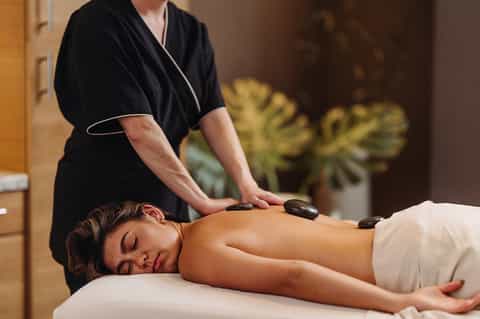 Spa therapist performing hot stone massage on relaxed client in wellness room