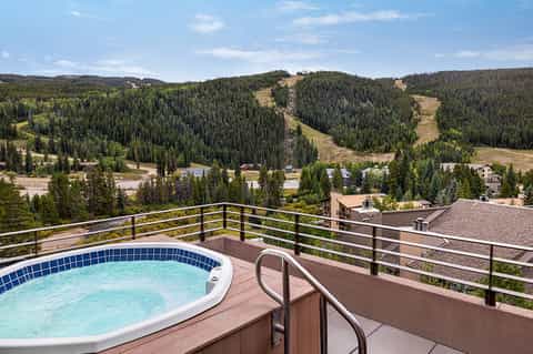 Hot tub on mountain overlook deck with forested hills and ski runs in background