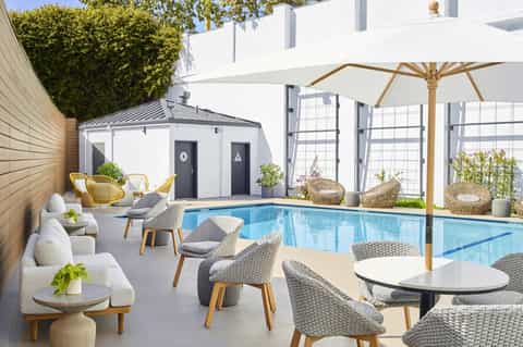 Luxurious indoor pool with woven lounge chairs, umbrellas, and modern white architecture surrounding the crystalline blue water.
