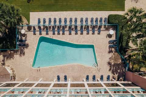 Overhead view of resort pool with lounge chairs arranged on beige patio surrounded by manicured grass