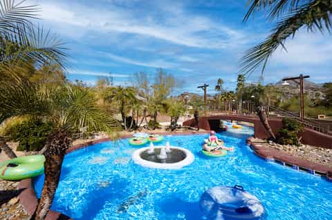 Bright blue lazy river pool with palm trees and desert landscape in sunny resort setting