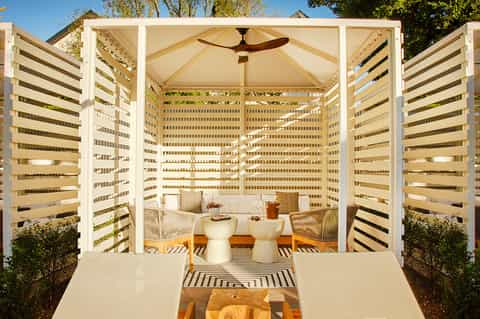Outdoor pergola lounge area with white lattice panels, cream seating, and striped rug