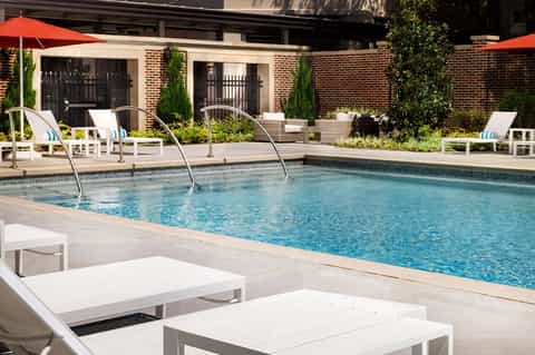 Luxury resort pool with brick building, loungers, umbrellas, and manicured landscaping