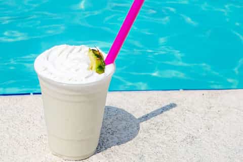 Frozen tropical cocktail with pineapple garnish and pink straw by swimming pool