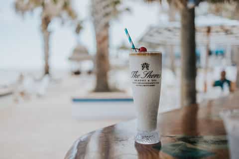 Frosted cocktail with cherry garnish at beachside resort bar with palm trees