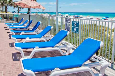 Row of blue and white lounge chairs on beachfront deck overlooking turquoise ocean