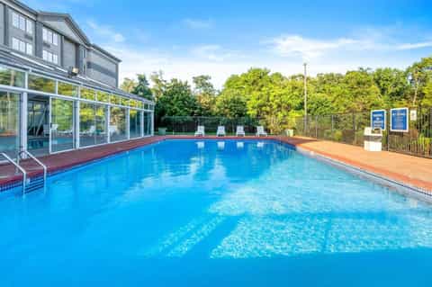 Indoor heated swimming pool with blue water, large windows, wooden deck, and surrounding trees
