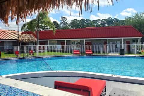 Resort pool with red metal roof building, white railings, lounge chairs, and tropical landscaping under blue sky