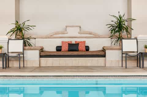 Luxury poolside lounge area with built-in seating, orange pillows, potted plants, and turquoise pool