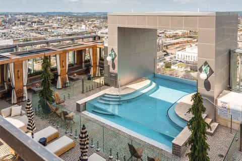 Luxury rooftop pool with blue water and city skyline views, featuring lounge areas and cabanas