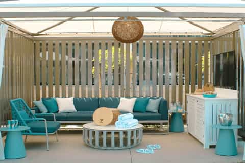 Modern outdoor lounge with turquoise sofa, round coffee table, and decorative ceiling structure