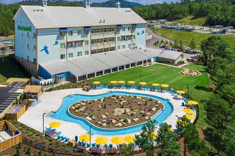 Aerial view of blue resort building with kidney-shaped pool surrounded by yellow umbrellas and manicured grounds