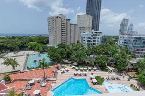 Aerial view of resort with multiple pools, sun loungers, and coastal backdrop with high-rise buildings