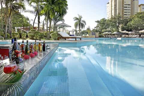 Luxury resort pool with palm trees, loungers, umbrellas, and tropical landscaping under clear sky