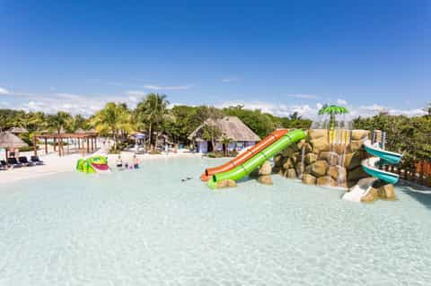 Shallow lagoon-style pool with colorful water slides and rock formations, palm trees in background