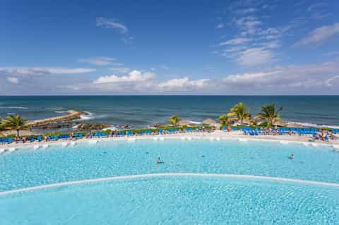Resort pool with turquoise water, lounge chairs, palm trees, and ocean view in background