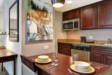 Modern kitchen and dining area with dark wood cabinetry, granite countertops, and palm tree artwork on beige walls