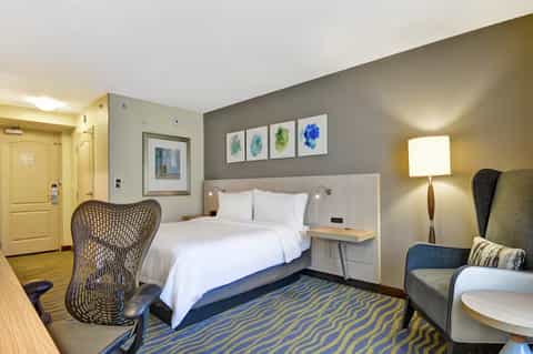 Modern hotel bedroom with queen bed, gray headboard, colorful abstract wall art, and contemporary furnishings