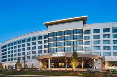 Modern Westin hotel exterior with curved white facade, gold trim, and illuminated entrance at dusk