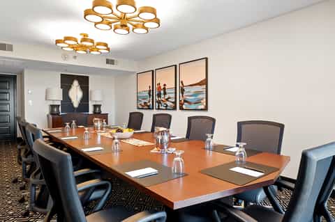 Modern conference room with long wooden table, black mesh chairs, and colorful beach artwork
