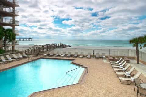 Beachfront resort pool with lounge chairs overlooking ocean and wooden pier