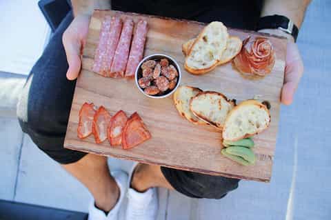 Charcuterie board with cured meats, bread, prosciutto rose, and sun-dried tomatoes on wooden serving platter