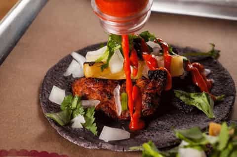 Charred meat dish with roasted vegetables and red pepper sauce on dark plate