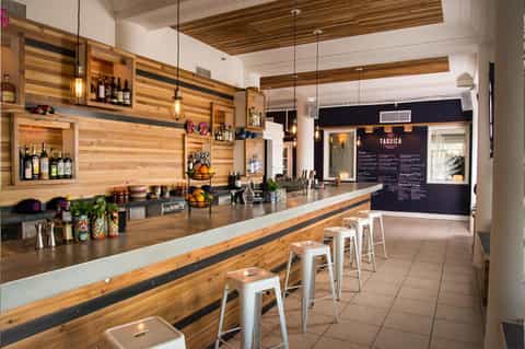 Modern bar interior with wooden striped walls, pendant lighting, and white metal bar stools along counter
