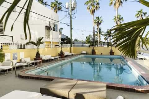 Yellow-walled resort courtyard with rectangular swimming pool, white lounge chairs, and palm trees under clear sky