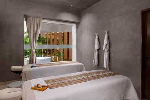 Spa treatment room with massage bed, wooden accents, natural light, and towel racks