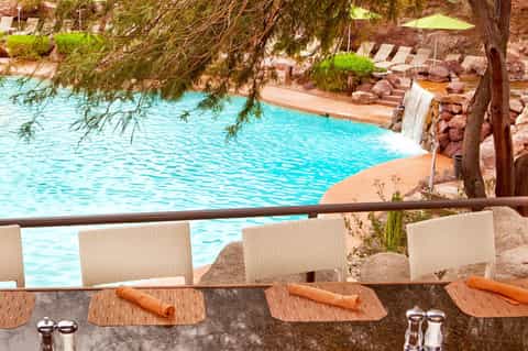 Resort pool area with turquoise water, waterfall feature, lounge chairs, and tree shade