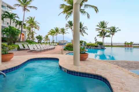 Resort pool area with lounge chairs, palm trees, and multi-level pools overlooking the waterfront