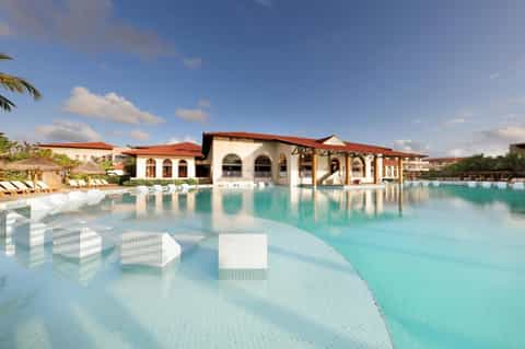 Turquoise resort pool with white loungers and Mediterranean-style buildings with terracotta roofs
