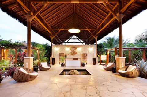 Luxury resort spa pavilion with wooden architecture, woven chairs, and stone fireplace surrounded by tropical plants