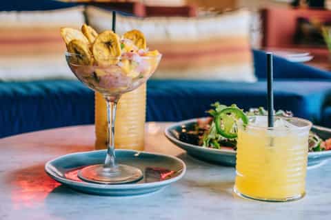 Tropical cocktails with plantain chips and jalapeño garnish on restaurant table with colorful cushioned seating