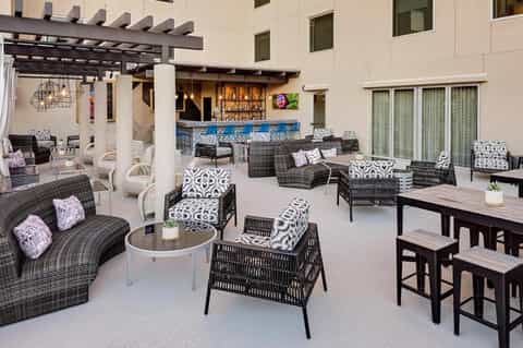 Upscale outdoor patio with wicker lounge chairs, patterned cushions, bar, and dining tables