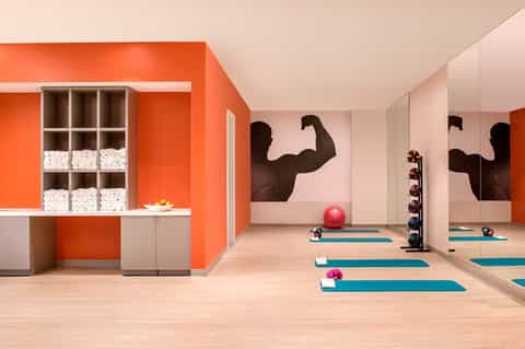 Modern fitness studio with orange accent wall, mirrors, and exercise equipment