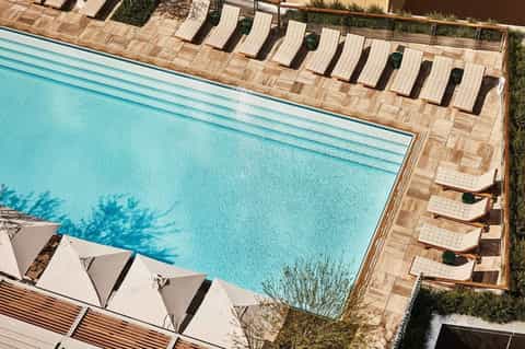 Overhead view of resort pool with lounge chairs on wooden deck and white umbrellas