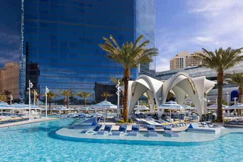 Luxury resort pool with white sail-shaped cabanas, palm trees, and modern blue glass towers