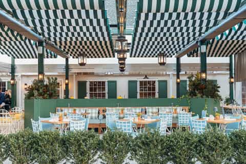 Outdoor dining area with green and white striped pergola, wooden tables, and light blue chairs