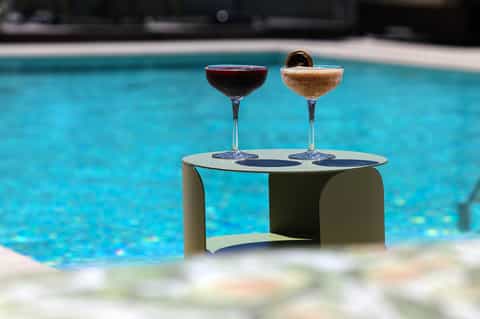 Two elegant cocktails on a white table beside a turquoise swimming pool