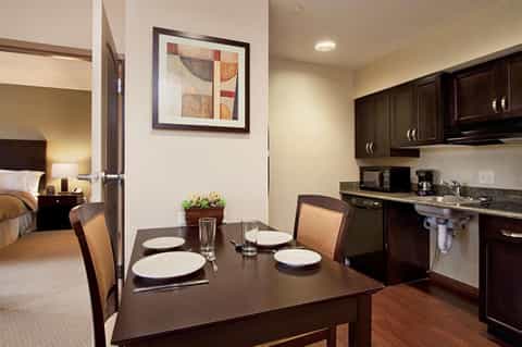 Hotel suite dining area with dark wood table, place settings, and open kitchen visible through doorway