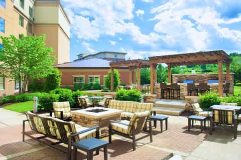Outdoor courtyard with fire pit seating area, striped cushioned chairs, wooden pergola, and resort building backdrop