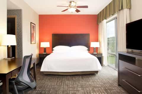 Modern hotel bedroom with vibrant orange accent wall, dark wood headboard, white bedding, and contemporary furnishings