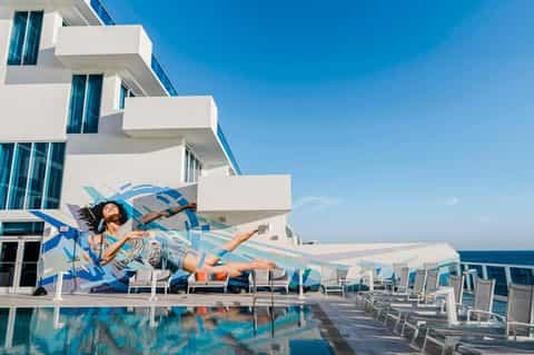 Woman relaxing on poolside lounge chair at oceanfront resort with white building