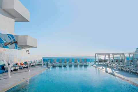 Modern rooftop infinity pool with ocean views, white loungers, and contemporary architecture