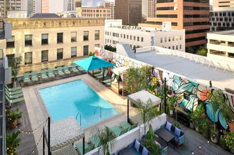 Urban rooftop pool with blue water, lounge chairs, and colorful graffiti art wall with city skyline